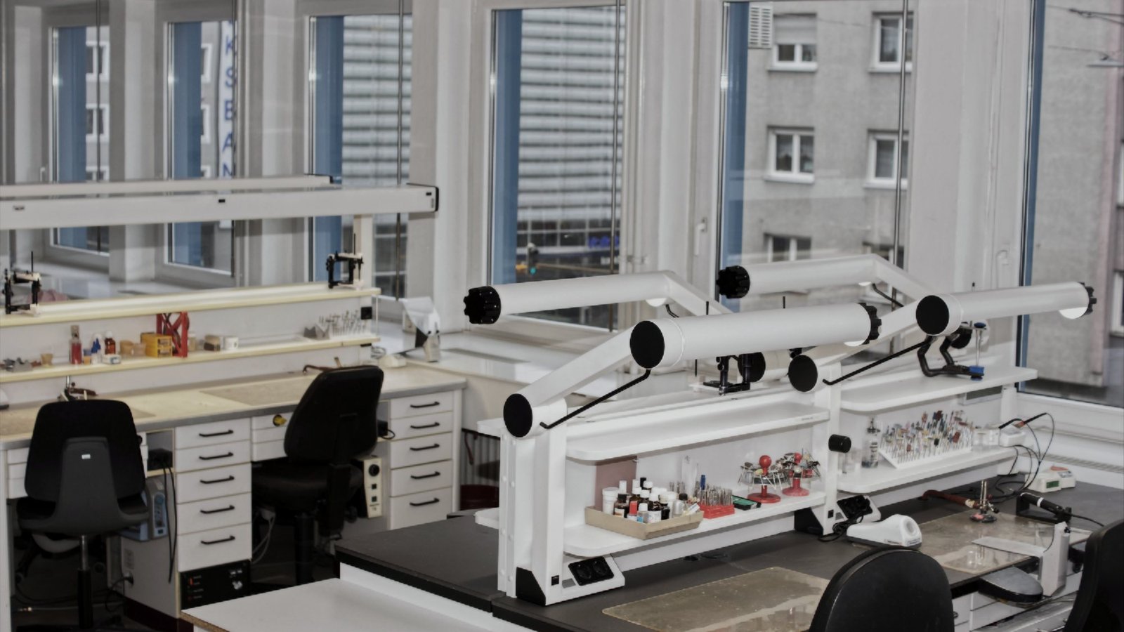 Blick in die Werkstatt: mehrere eingerichtete Arbeitsplätze mit Gelenkleuchten und Tageslicht von der Fensterseite.
